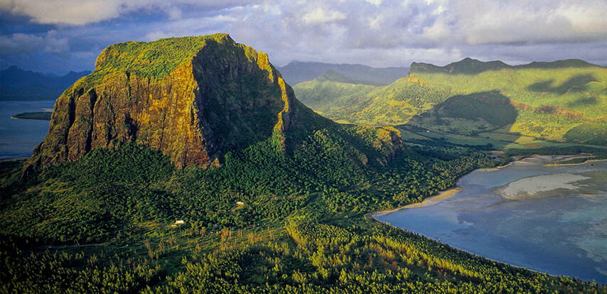 A stunning aerial view of Le Morne Brabant Mountain in Mauritius, showcasing its dramatic cliffs, lush greenery, and surrounding blue lagoon waters - start your journey with JKV Travel.